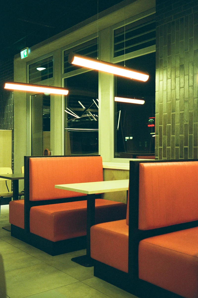 An empty diner after dark, photographed on film, with orange booths beneath warm hanging lights.