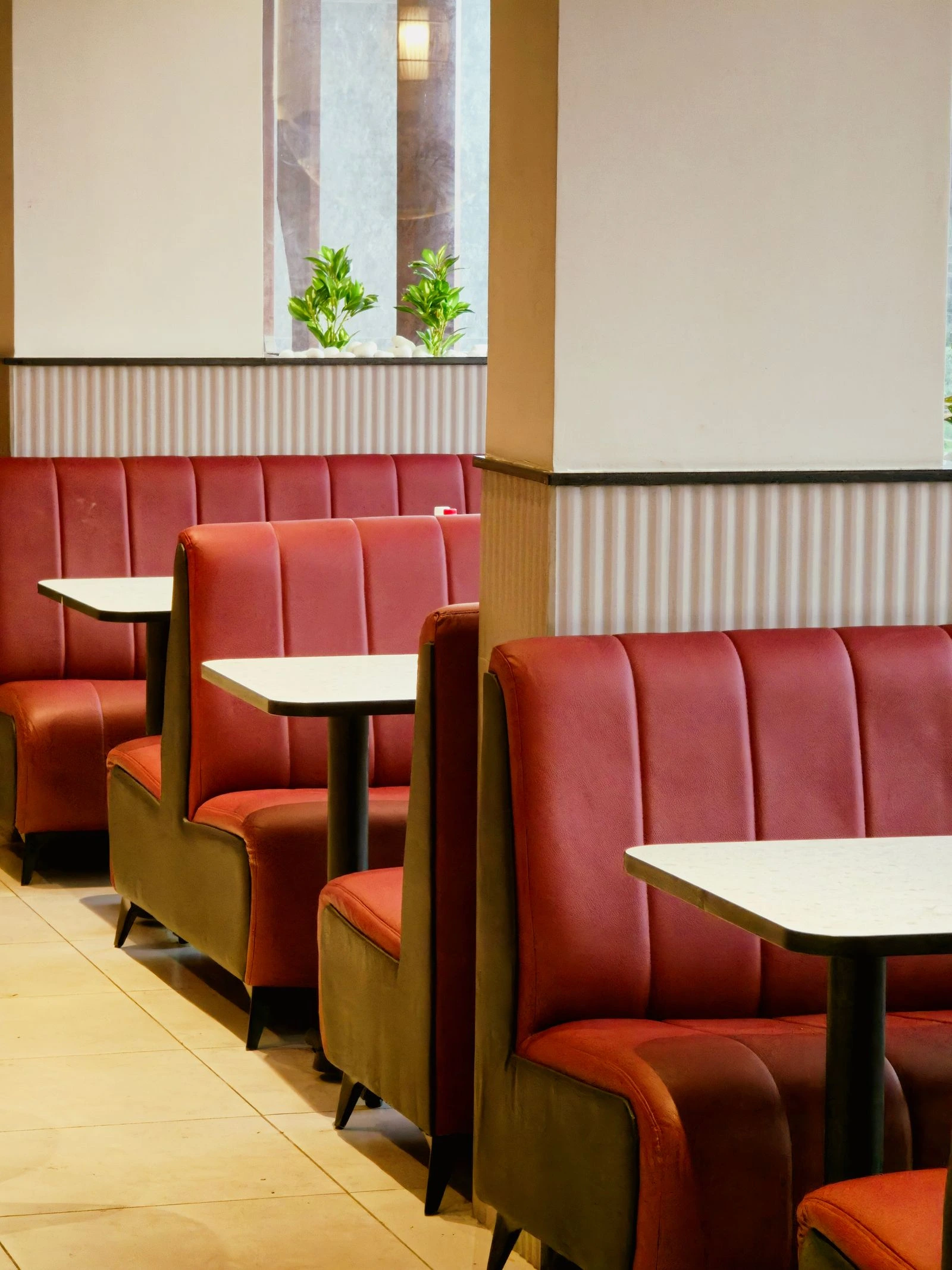 Empty red vinyl diner booths, with worn seats and afternoon light falling across the tables.